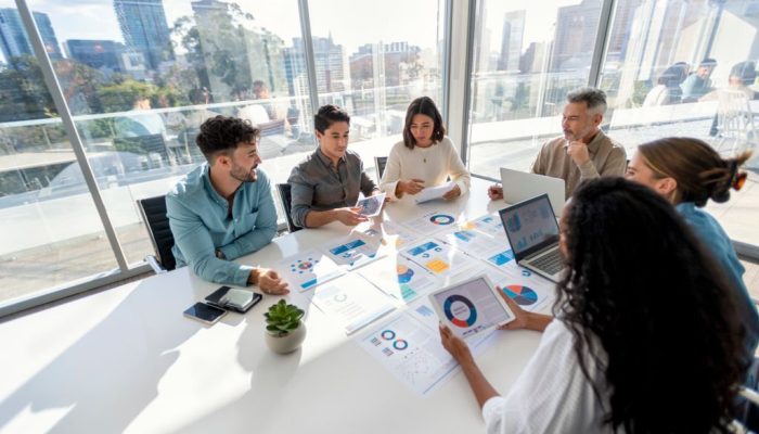 Multi racial group of people working with Paperwork on a board room table at a business presentation or seminar. The documents have financial or marketing figures, graphs and charts on them. There is a laptop and digital tablet  on the table. Multi ethnic group including Caucasian and African American